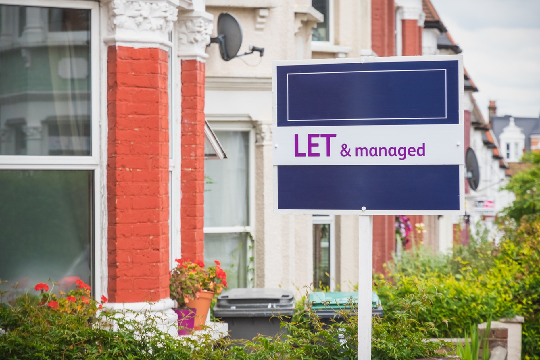 A “Let & managed” real estate sign in front of a row of residential houses with red brick columns, windows, and small front gardens.