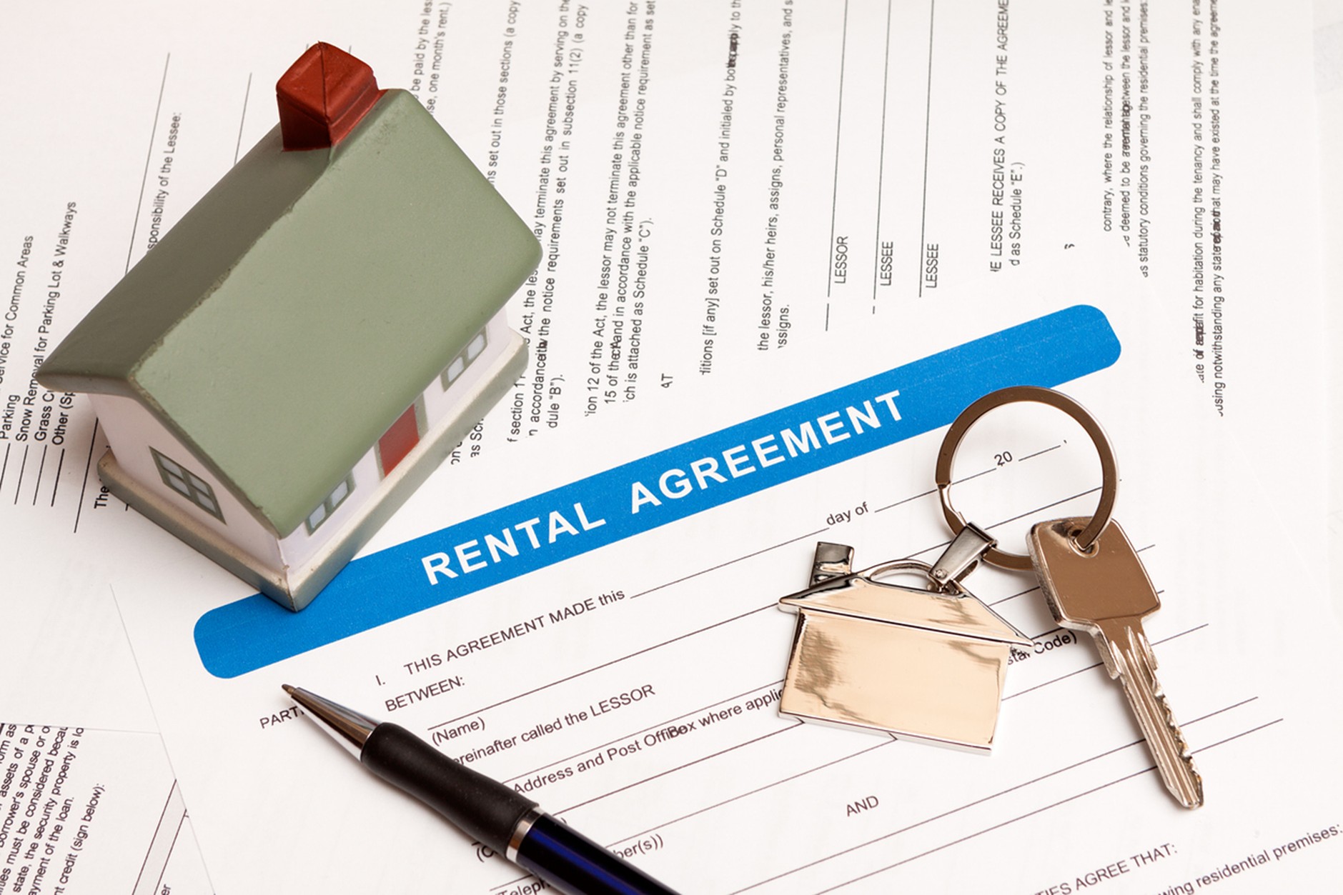 op-down view of a rental agreement document with a pen, a set of keys with a house-shaped keychain, and a small model house placed on top, symbolizing a property lease.