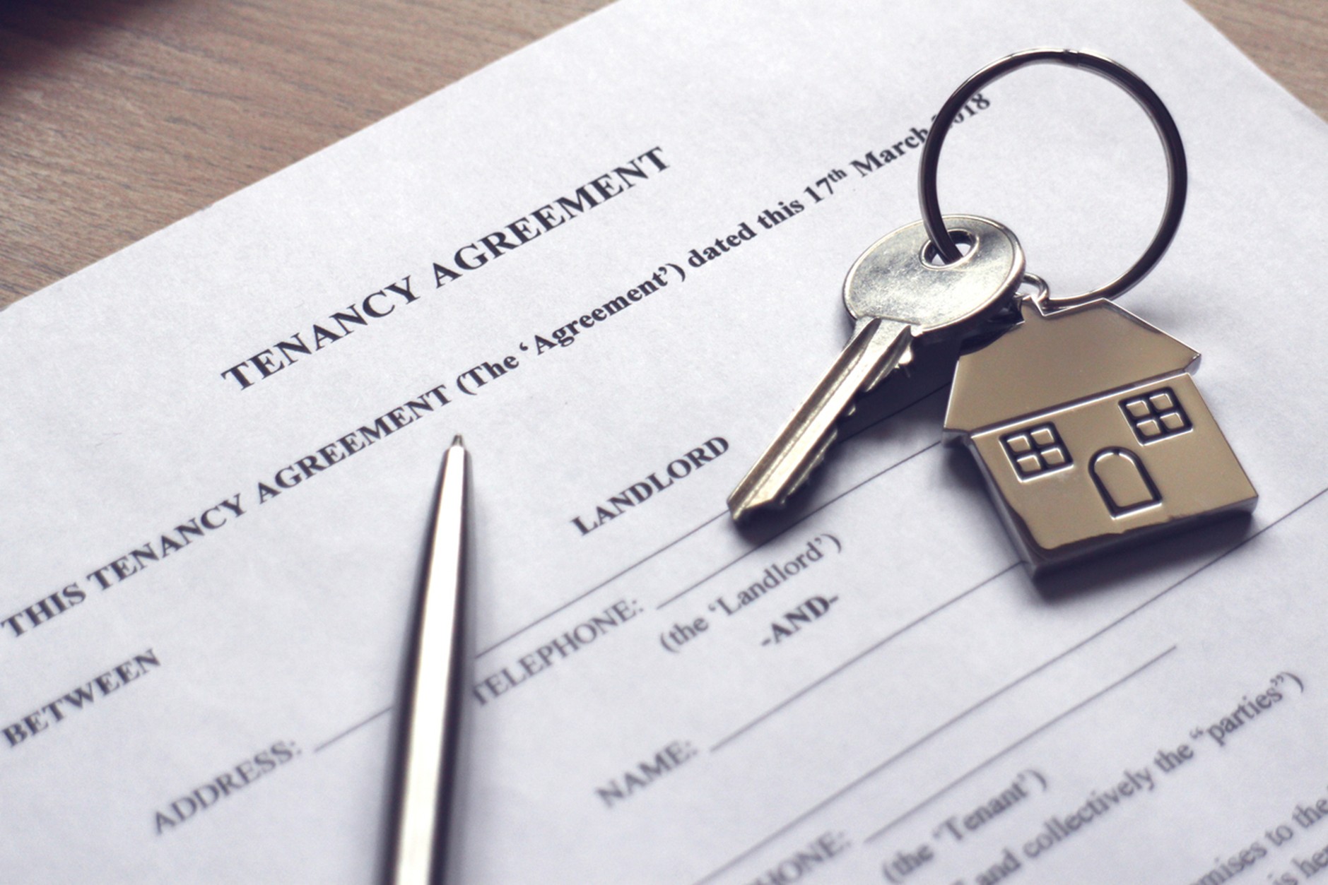 Close-up of a tenancy agreement document on a desk with a pen and a set of keys featuring a house-shaped keychain, suggesting signing a rental contract.